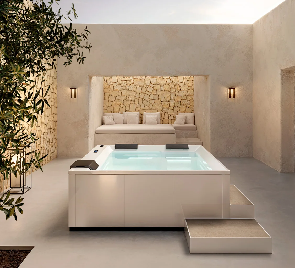 Gruppo Treesse Wave GP, een vierkante witte spa met opstap op een binnenplaats met een natuurstenen muur